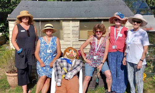 A group of Budding Friends volunteers in front of the allotment shed, with their scarecrow